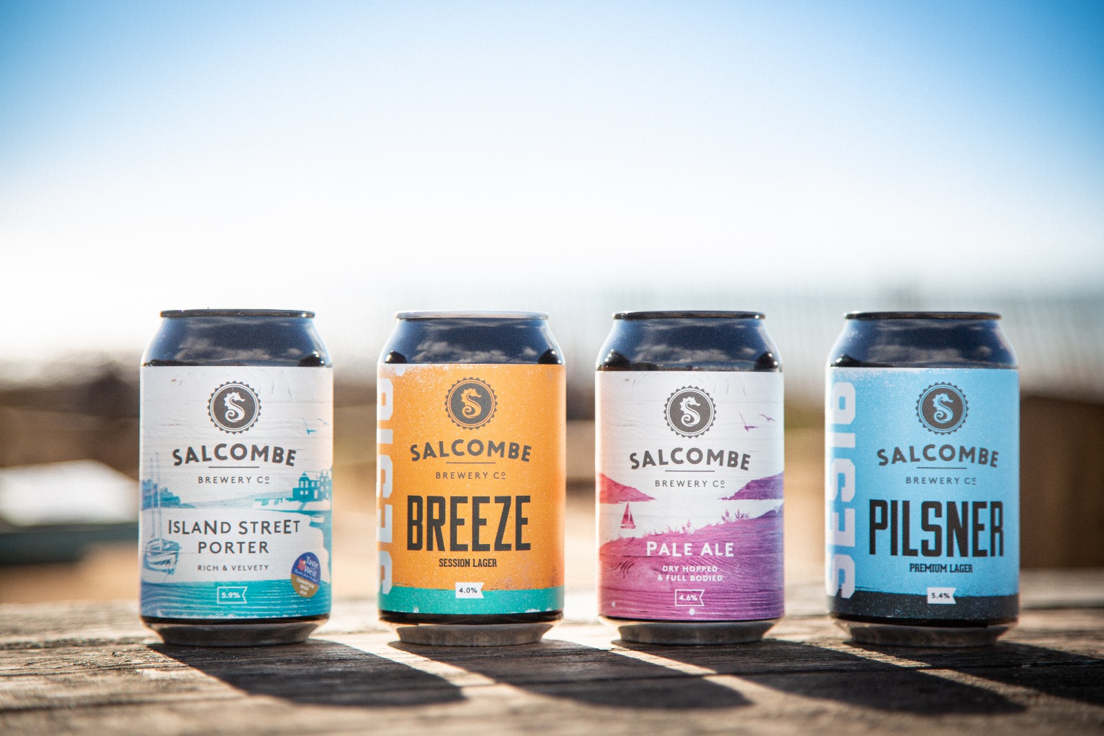 Cans of Salcombe Brewery beers Island Street Porter, Breeze, Pale Ale and Pilsner. Beach in background.